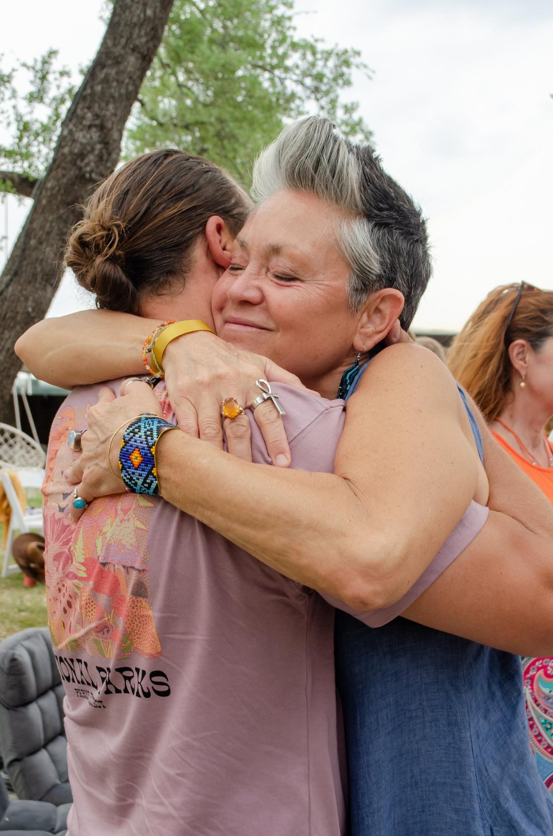 Two women at an AUREA gathering holding each other, eyes closed.