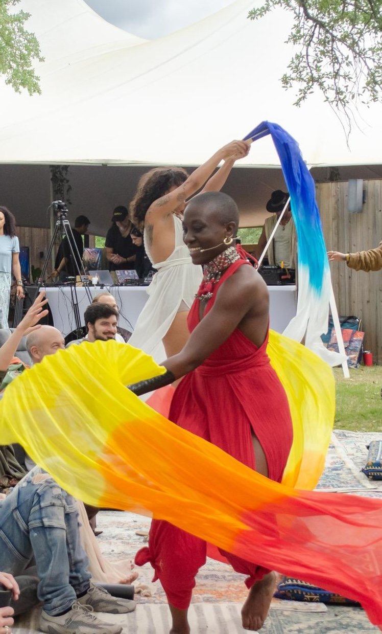 A dancer in red spinning colored silks before the seated gathering.